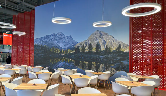 Grosses Panoramafoto einer Morgenstimmung an einem Bergsee im Verpflegungsteil eines Messestandes.